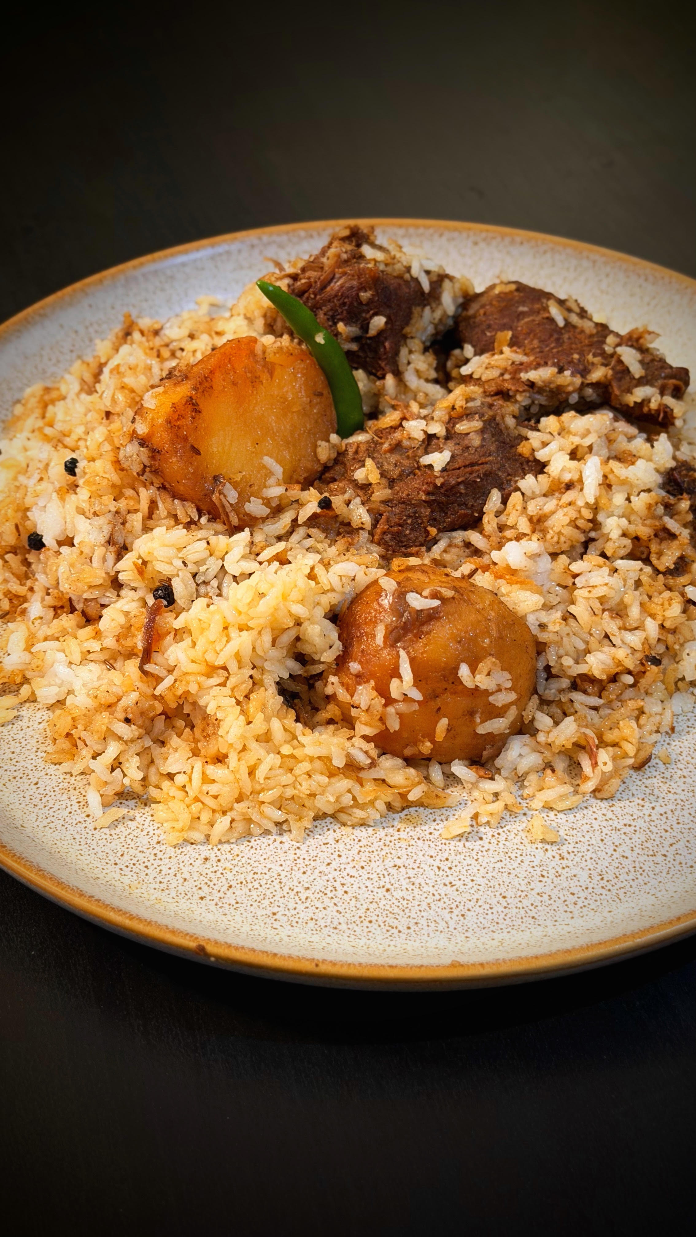 A plated serving of beef tehari with potato, egg, and green chili
