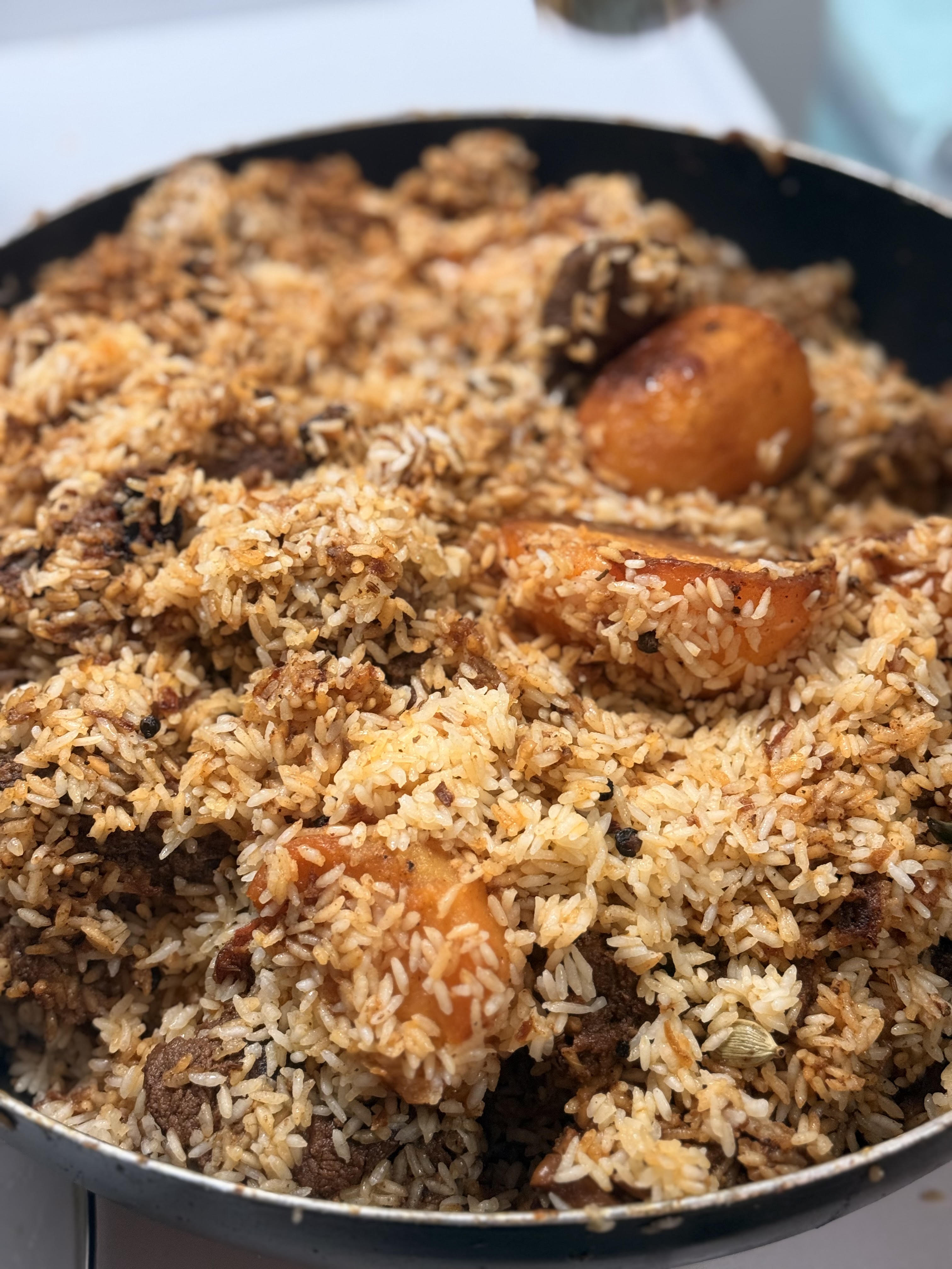 Biriyani cooking in a pan, garnished with fried potato and whole spices